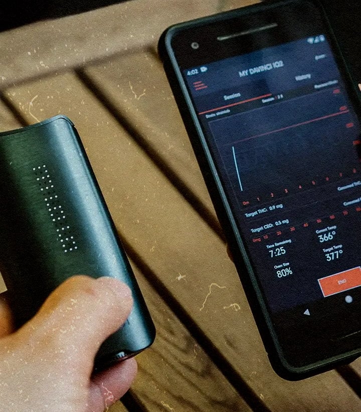 PAX IQ3 vaporizer with app showing 80% battery, THC 0.5mg, and 366°F temp, held next to a phone on a wooden table.