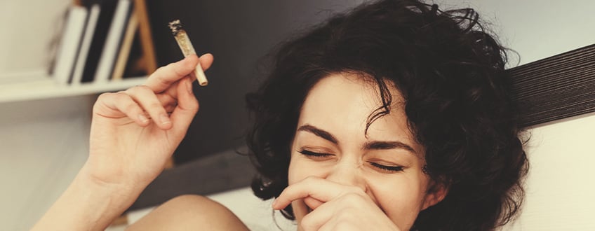 Person laughing while holding a cannabis joint.