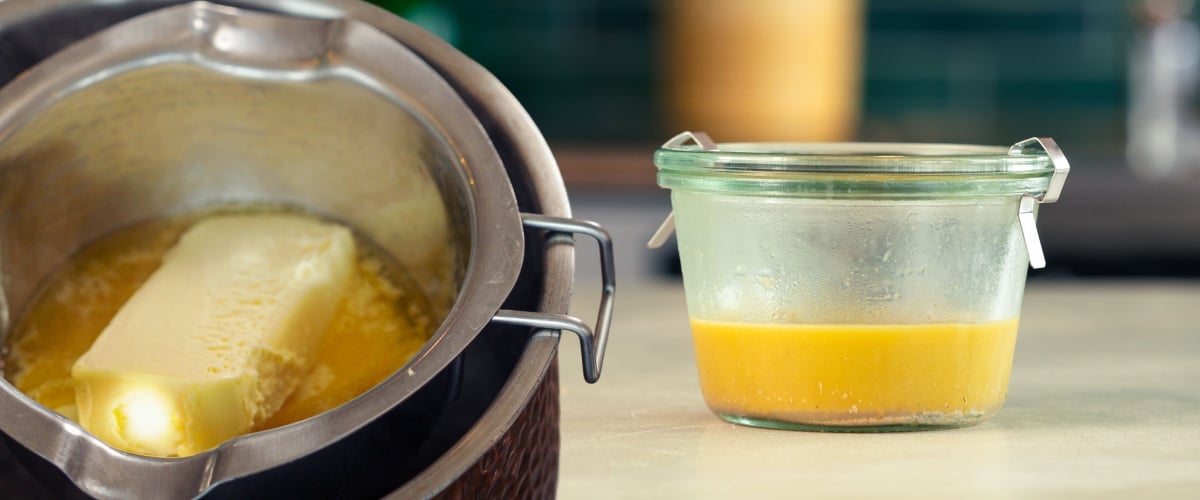 Melted cannabutter being prepared in a pot and transferred into a glass container on a kitchen counter.