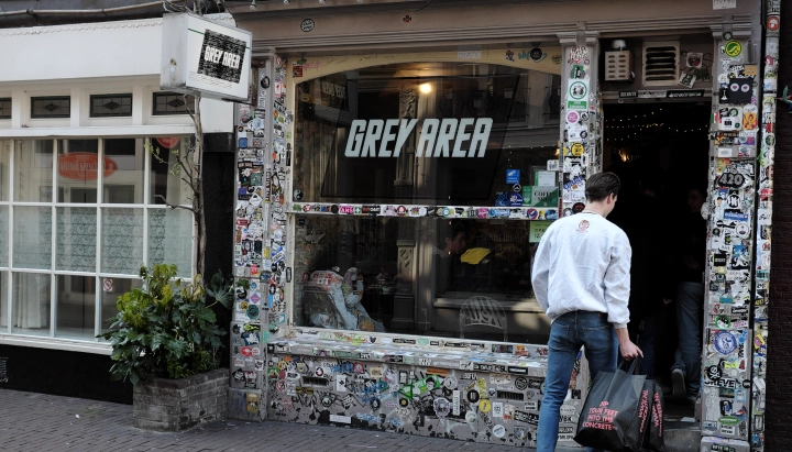 Cannabis Coffeeshop in the Netherlands Entrance of a cannabis coffeeshop in the Netherlands with a Grey Area sign and sticker-covered storefront.