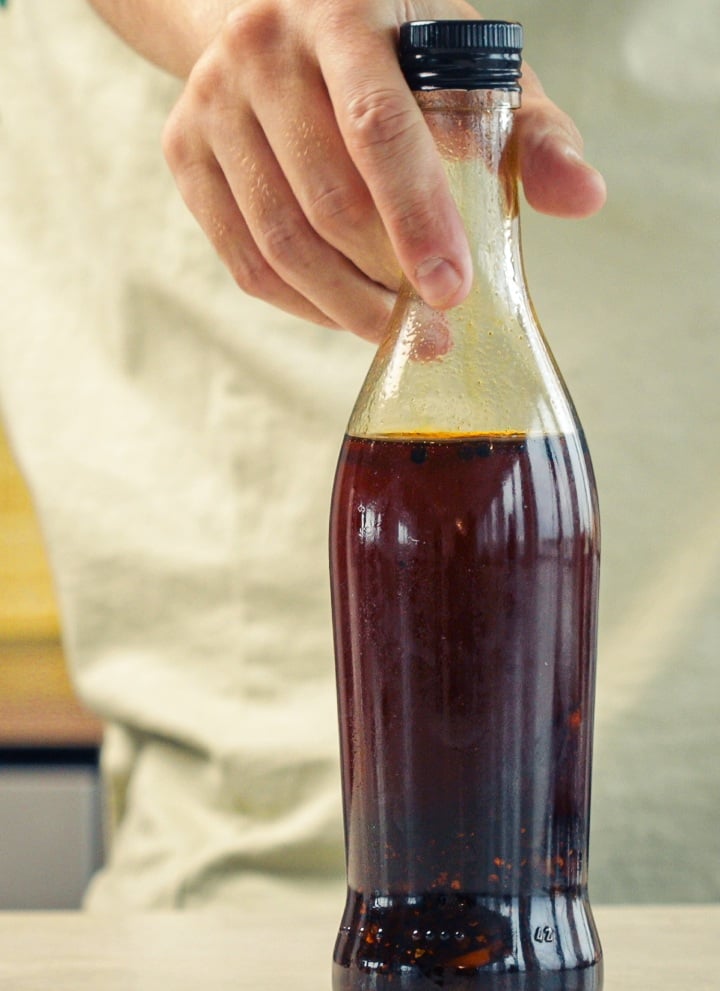 Sealed glass bottle filled with cannabis-infused chilli oil stored for preservation in a kitchen setting
