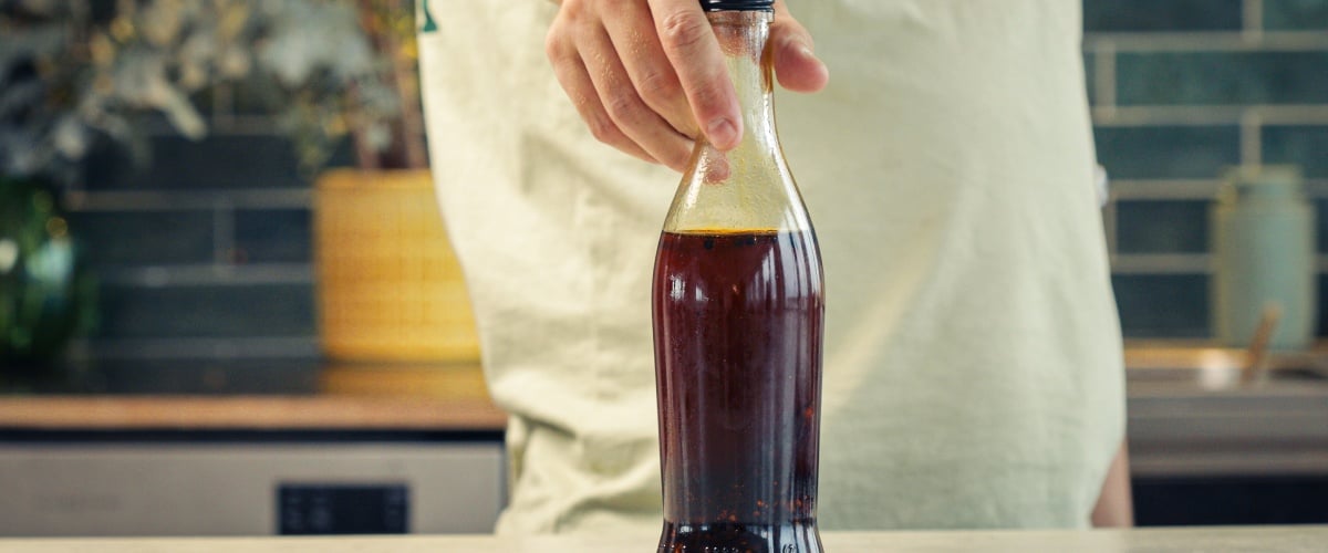 Sealed glass bottle filled with cannabis-infused chilli oil stored for preservation in a kitchen setting