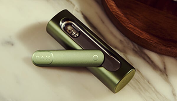 Opened Pax Flow Vaporizer Close-up of the opened Pax Flow vaporizer revealing its internal chamber packed with cannabis, held by a hand in a casual outdoor setting with natural light.