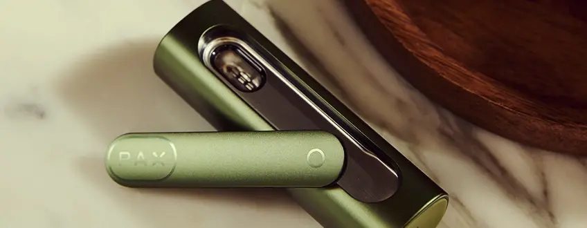 Opened Pax Flow Vaporizer Close-up of the opened Pax Flow vaporizer revealing its internal chamber packed with cannabis, held by a hand in a casual outdoor setting with natural light.