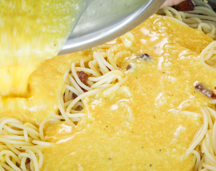 Pouring egg and cheese mixture over hot spaghetti in a pan, fifth step for making cannabis-infused carbonara sauce